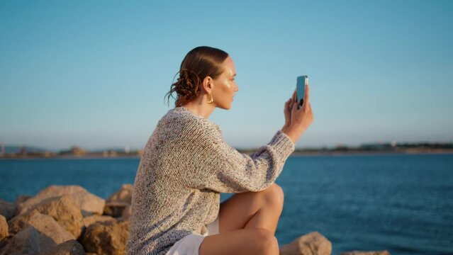 Coast girl taking pictures with smartphone in sunlight. Beautiful girl resting