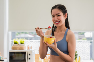 Beautiful Asian young female eating strawberry yogurt for health in the kitchen room at the apartment.