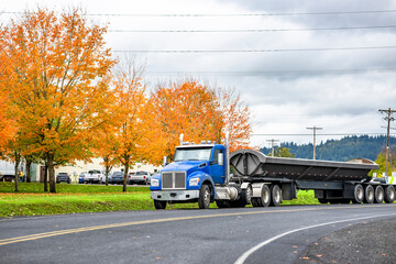 Tip truck blue big rig semi truck tractor with long tipper trailer standing on the road shoulder in...