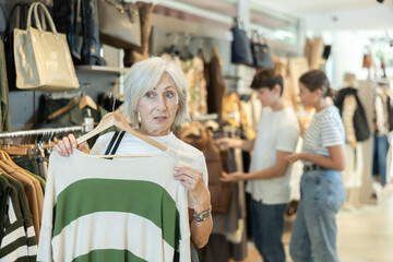 elderly lady carefully examines selection of sweaters, searching for ideal one to keep her warm.