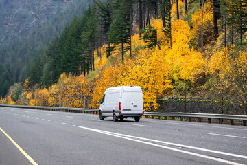 Cargo compact mini van driving on the scenic autumn highway road with yellow trees on the mountain hillside