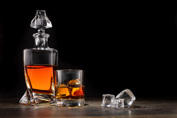 Bourbon decanter and glass on a wooden surface, with melting ice cubes nearby in a low key dark environment.