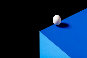 Egg on a vivid blue surface standing on the edge against a black background.