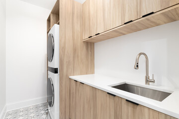 A laundry room with wood cabinets, a white marble countertop, patterned tile floor, and white washer and dryer. - obrazy, fototapety, plakaty