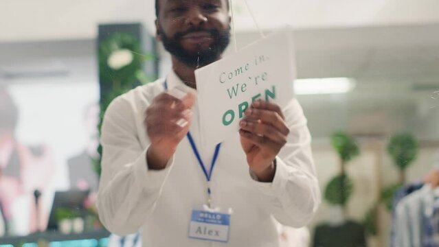 Smiling storekeeper finally reopening store after restocking elegant high end fashion boutique. Man turning closed sign from clothing store door after adding new collection, close up