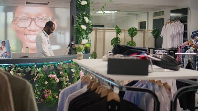 BIPOC man working in luxurious clothing store with elegant assortment of blazers. African american shopkeeper awaiting clients in premium fashion boutique with stylish attire garments