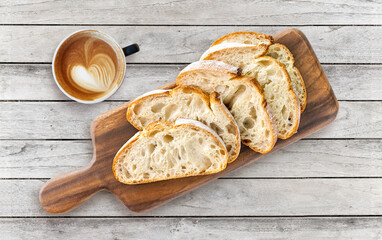 French ciabatta sliced bread, cup of coffee on a board and grey table