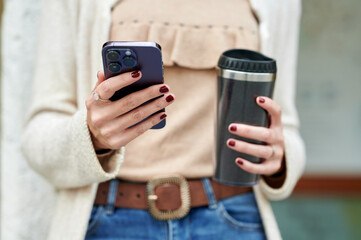 Close-up of woman's hands holding mobile phone and reusable cup