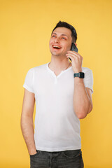 young man holding a phone, talking emotionally on the phone on a yellow background.