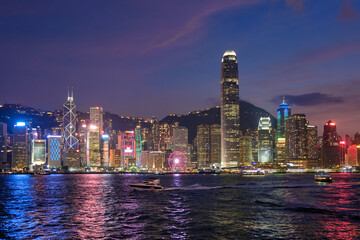 Hong Kong skyline cityscape downtown skyscrapers over Victoria Harbour in the evening illuminated with tourist boat ferries . Hong Kong, China