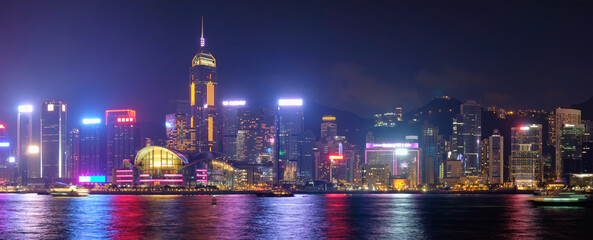 Fototapeta na wymiar Panorama of Hong Kong skyline cityscape downtown skyscrapers over Victoria Harbour in the evening illuminated tourist boats and ferries . Hong Kong, China