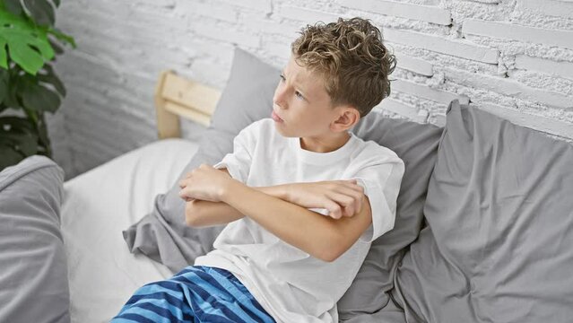 Adorable blond boy sitting in bedroom, scratching itchy arm rash - indoor allergy problem or eczema? child's health at stake in home environment!