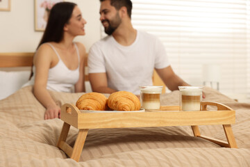 Obraz na płótnie Canvas Happy couple together on bed at home, focus on wooden tray with breakfast