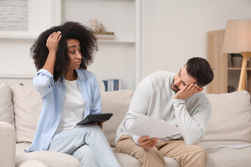 Confused couple with debt notifications and calculator planning budget at home. Financial problem