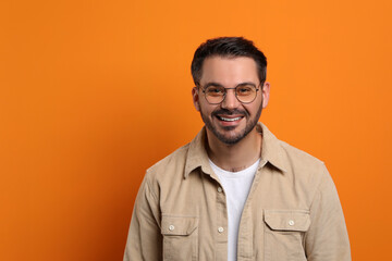 Portrait of smiling man in stylish glasses on orange background. Space for text