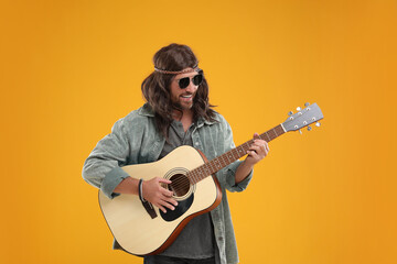 Stylish hippie man playing guitar on orange background - obrazy, fototapety, plakaty