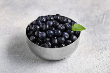 Ripe bilberries and leaf in bowl on light grey textured table