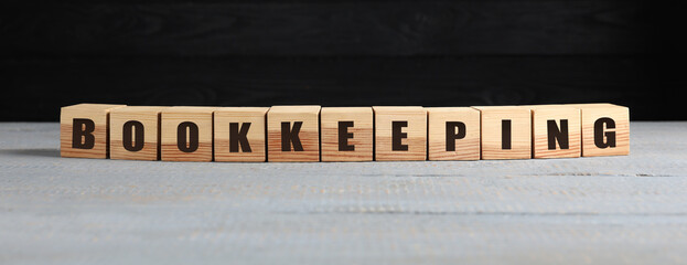 Word Bookkeeping made with cubes on light grey wooden table against black wall. Space for text