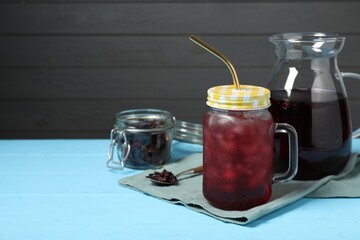 Delicious iced hibiscus tea and dry flowers on light blue wooden table, space for text