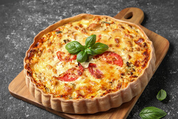 Tasty quiche with tomatoes, basil and cheese on dark textured table, closeup