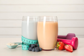 Tasty shakes with berries, dumbbells, measuring tape and powder on light wooden table. Weight loss