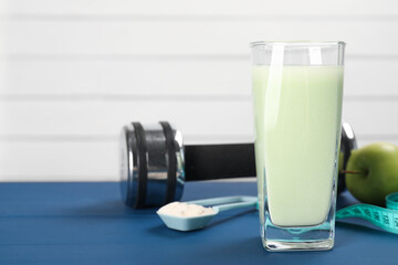 Tasty shake, dumbbell, measuring tape, powder and apple on blue table, closeup with space for text....