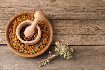 Mortar with pestle, many different dry herbs and flowers on wooden table, flat lay. Space for text