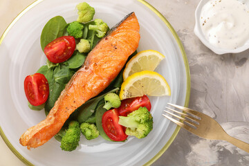 Healthy meal. Piece of grilled salmon, vegetables, lemon and spinach served with sauce on light grey textured table, flat lay
