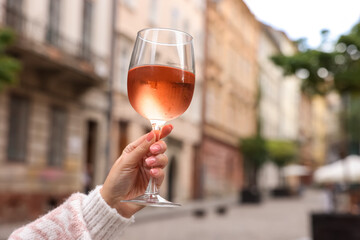 Woman holding glass of rose wine outdoors, closeup. Space for text