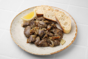 Tasty fried chicken liver served with lemon and bread on white tiled table, closeup