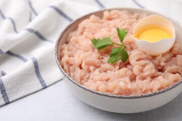 Fresh raw minced meat, parsley and egg in bowl on light grey table, closeup. Space for text