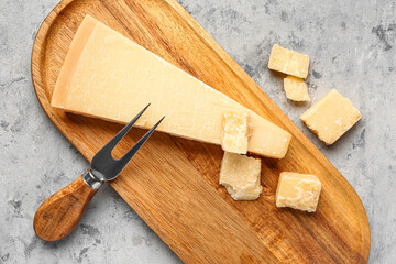 Wooden board with pieces of tasty Parmesan cheese on grunge background, closeup