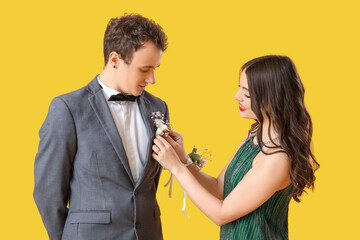 Beautiful prom couple pinning boutonniere on yellow background