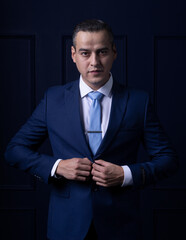 White Mexican man dressed in blue suit fastening the button on his jacket looking at the camera