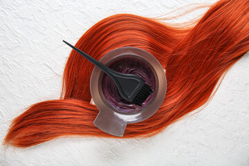 Bowl with hair dye, brush and ginger strand on white background