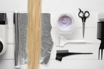 Bowl with hair dye, set of hairdresser's tools and blond strand on white wooden background
