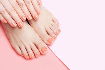 Female hands and feet with manicure and pedicure on pink background close-up, top view.