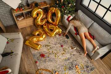 Drunk woman lying on sofa in messy living room after New Year party