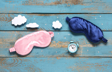 Composition with sleep masks, paper clouds and alarm clock on color wooden background