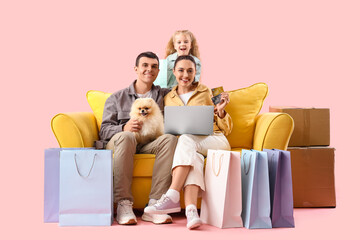 Happy family with laptop and shopping bags sitting on sofa against pink background