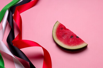 Colorful ribbons, red, black, green, white and slice of watermelon on pink background