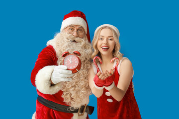 People dressed as Santa Claus with alarm clock and candy canes on blue background