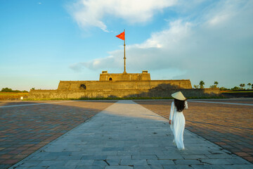 Ky Dai flag tower at Ngo Mon square with Vietnamese girl wearing traditional dress Ao Dai in the Imperial Place in Hue city, Vietnam. Famous travel destination