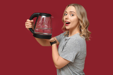 Beautiful young woman with modern electric kettle on red background