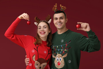 Beautiful young couple in reindeer horns with Christmas balls on red background