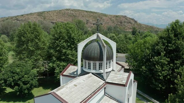 Pedestal drone shot of St Petka Church's dome, and slowly orbitting around the rest of the buildings around the church, revealing  the surrounding trees and mountains.