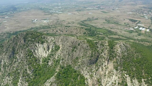 Pull-away drone shot retreating slowly from the mountain showing the rest of the different surrounding landforms like the fields and plains in the nearby town of Rupite in Petrich, Bulgaria.