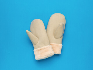 Insulated beige mittens with fur on a blue background.