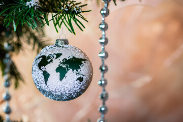Christmas glass sphere with a figure in the shape of a world map hanging from a pine branch.