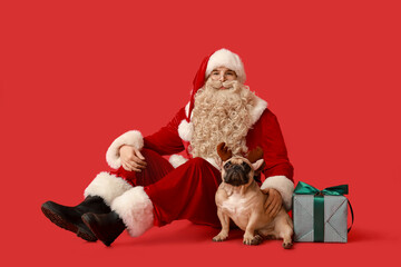 Santa Claus with Christmas gift and French bulldog in reindeer horns on red background